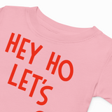 Pink t-shirt with red text 'HEY HO LET'S' on a white background