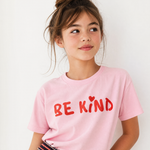 Young girl wearing a pink t-shirt with 'BE KIND' text on a white background
