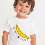 A smiling toddler wearing a white short-sleeve t-shirt with a yellow banana graphic and the words 'CUCKOO BANANAS' in colorful letters, paired with light-colored patterned shorts against a plain white background.