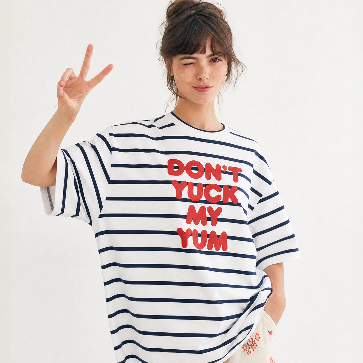 Woman wearing a striped t-shirt with text, making a peace sign.