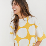 Woman wearing a yellow and white polka dot top against a white background