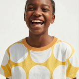 Child wearing a yellow shirt with white polka dots, smiling against a plain background