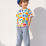 Child wearing a colorful shirt with abstract patterns and striped pants on a white background