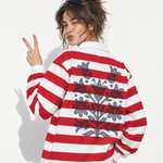 Woman making peace sign, wearing an oversized red-and-white striped rugby shirt with graphic print on the back.