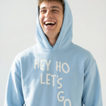 Person wearing a light blue hoodie with 'HEY HO LET'S GO' text on a plain background