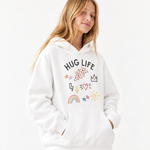 A woman wearing a white pullover hoodie with a colorful graphic print that reads 'HUG LIFE' and includes stars, flowers, a rainbow, lightning bolts, and hearts, set against a plain white background.