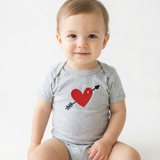Baby wearing a gray onesie with a red heart and black arrow design on a white background