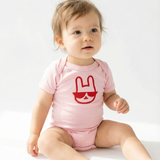 Baby wearing a pink onesie with a red graphic on a white background