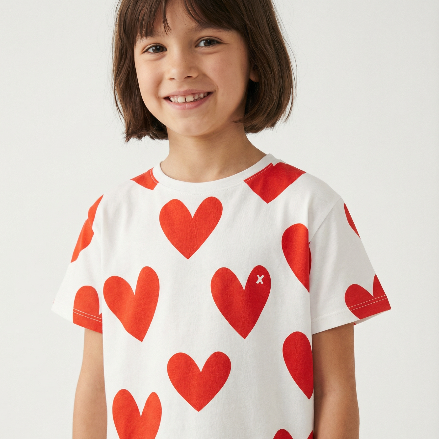 Child wearing a white t-shirt with red heart patterns on a plain background