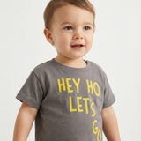 Child wearing a gray t-shirt with yellow text on a plain background