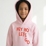 Child wearing a pink hoodie with 'HEY HO LET'S GO' text on a white background