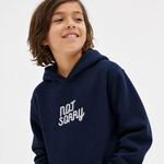A smiling young boy with brown hair wearing a navy blue hoodie with 'NOT SORRY' embroidered in white script on the chest, set against a plain light gray background.
