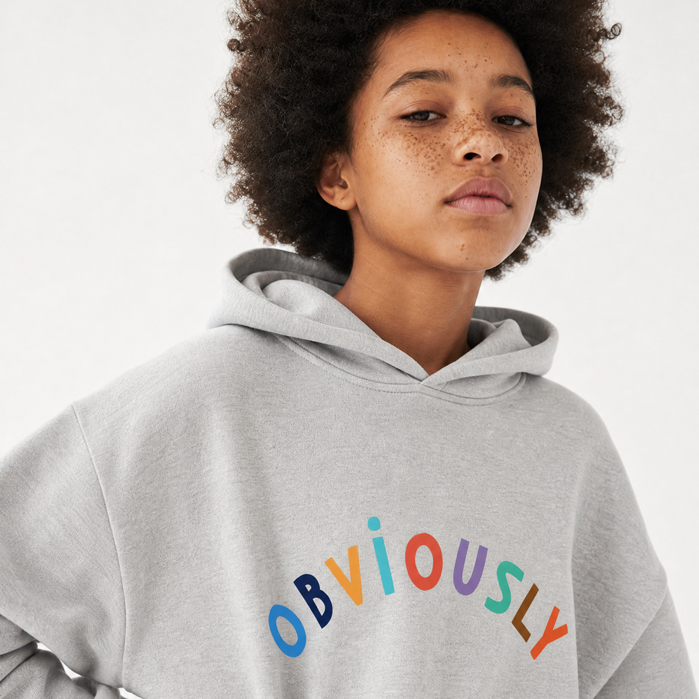 A close-up of a person wearing a light gray hoodie with the word 'OBVIOUSLY' printed across the chest in colorful lowercase letters, against a plain light background.
