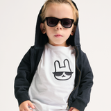 Child wearing sunglasses and a black and white outfit with a rabbit design on a light gray background