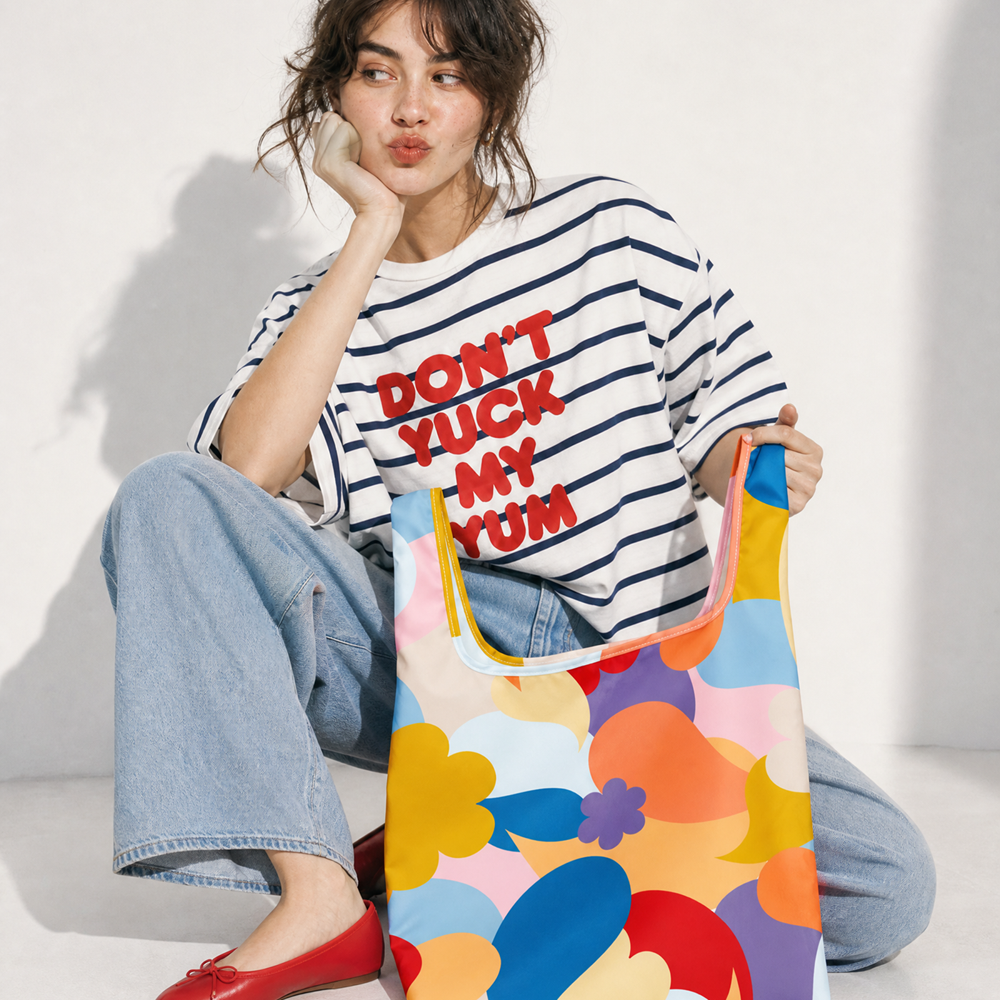 Woman holding a colorful tote bag wearing a striped shirt with text.