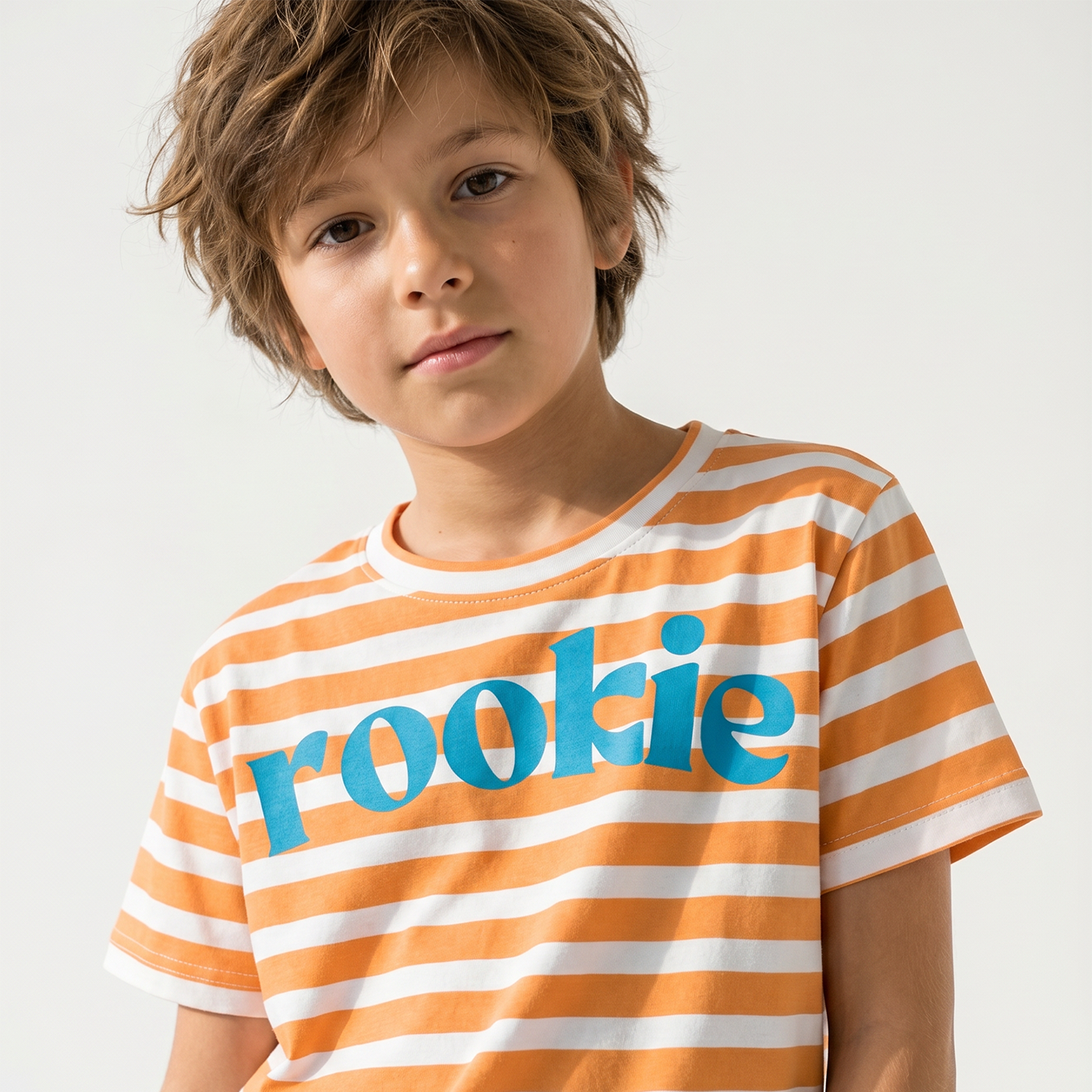 Child wearing an orange and white striped shirt with the word 'rookie' on a plain background