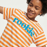 Child wearing an orange and white striped shirt with the word 'rookie' on a light background