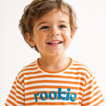 A smiling young boy with brown hair wearing a short-sleeve orange and white striped t-shirt with the word 'rookie' printed in blue across the chest, set against a plain white background.