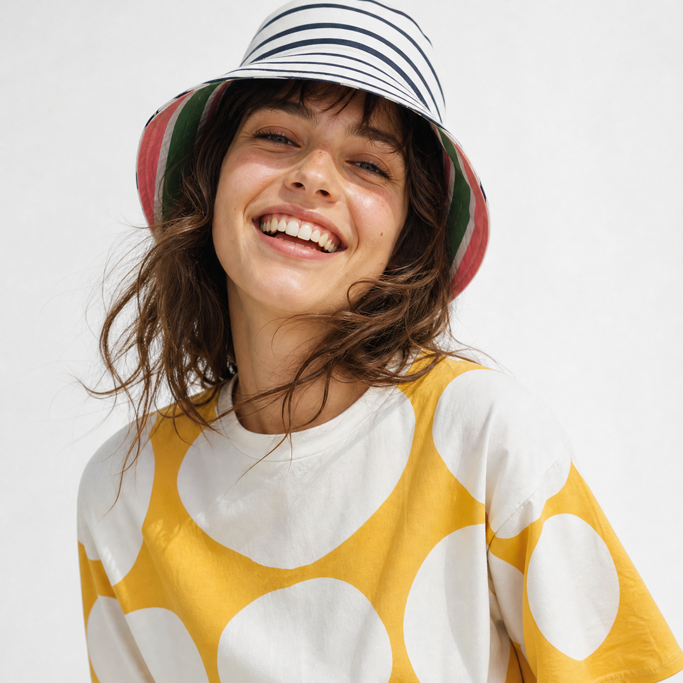 Woman wearing a colorful bucket hat and a yellow polka dot shirt on a white background