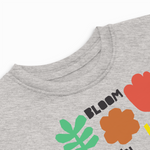 Close-up detail of a heather gray toddler T-shirt showing the ribbed neckline and colorful "Bloom" floral graphic with a red tulip, orange flower, and green leaf.
