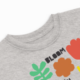 Close-up detail of a heather gray toddler T-shirt showing the ribbed neckline and colorful "Bloom" floral graphic with a red tulip, orange flower, and green leaf.