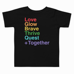 A black toddler short-sleeve t-shirt with a colorful stacked text graphic on the chest reading 'Love Glow Brave Thrive Quest +Together' in rainbow colors, shown against a plain white background.