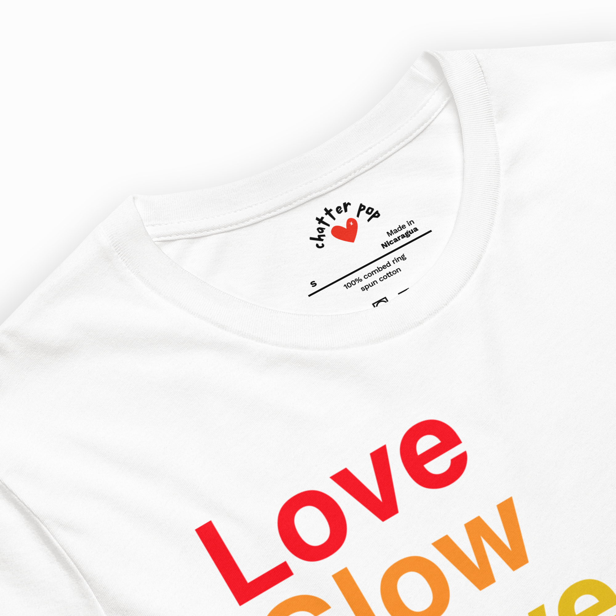 Close-up of a white short-sleeve t-shirt showing the inner neck label with 'clutter pop' and a red heart logo, alongside a colorful graphic print of the word 'Love glow' in red, orange, and yellow.