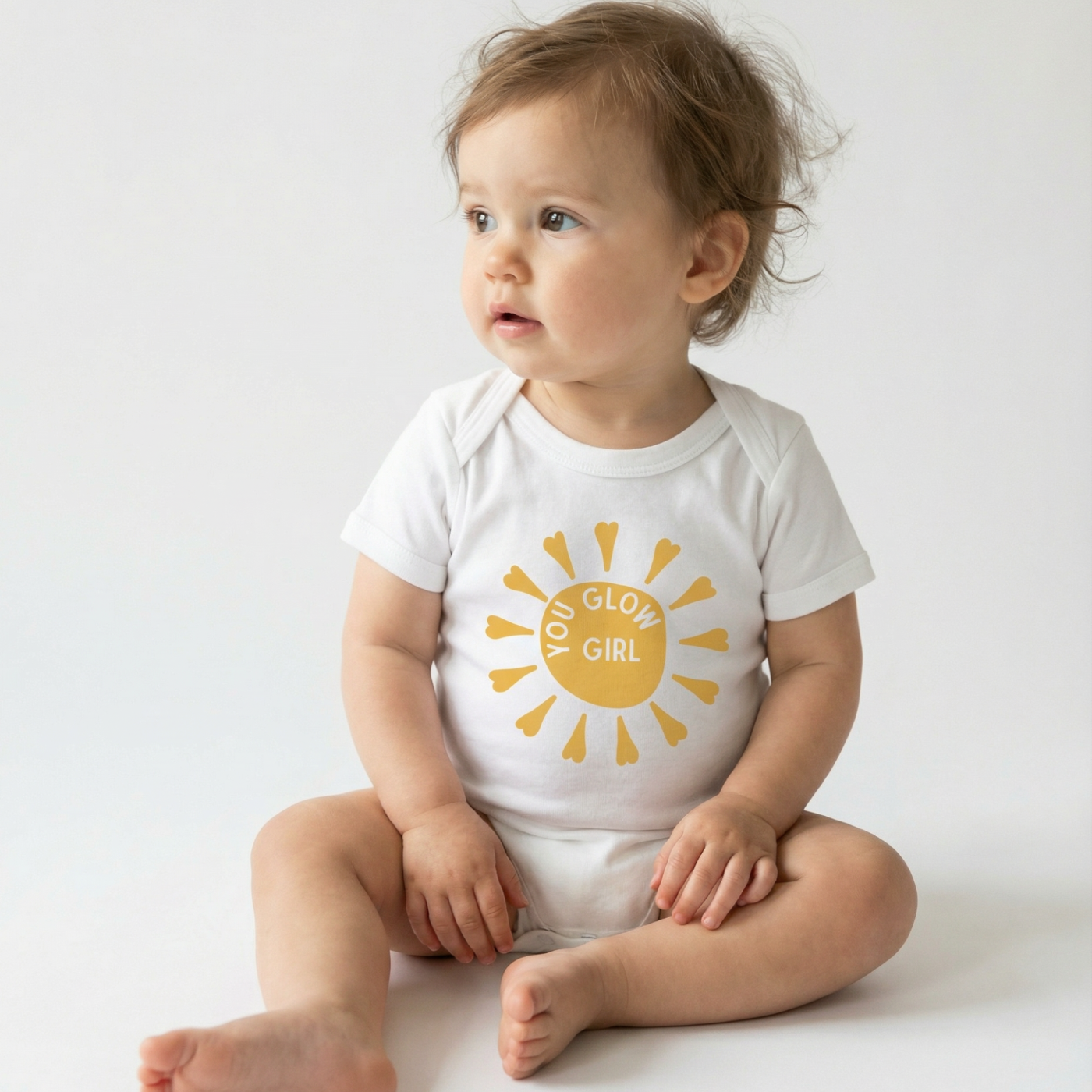 Baby wearing a white onesie with a yellow sun design and text on a plain background