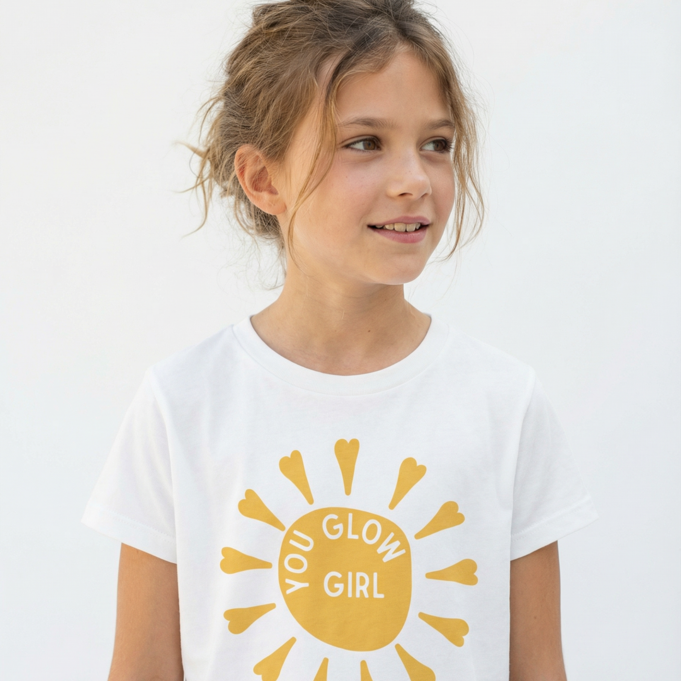 Young girl wearing a white t-shirt with a yellow sun design and text on a plain background